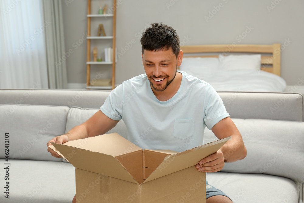 Happy man opening parcel on sofa at home. Internet shopping Happy man opening parcel on sofa at home. Internet shopping