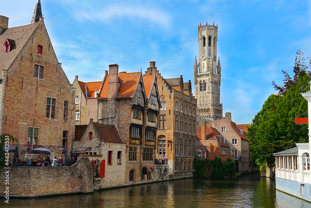 view of the famous dijver canal with historic buildings alongside the watercourse and view of the belfry tower in the center of bruges, Flanders, belgium