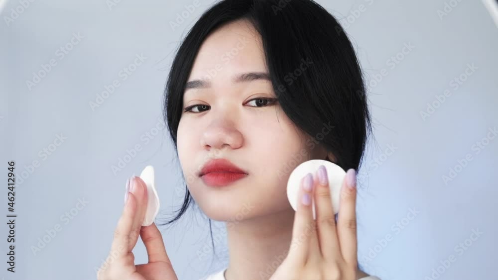 Face toner. Skin care. Beauty cosmetology. Cleansing freshness. Charming Vietnamese woman applying facial moisturizing product with cotton pads isolated on light background. Face toner. Skin care. Beauty cosmetology. Cleansing freshness. Charming Vietnamese woman applying facial moisturizing product with cotton pads isolated on light background.