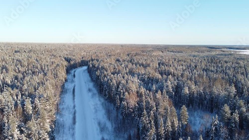 Aerial view from a drone of a road in the middle of snow-covered trees and snow-covered forest on a winter day. A dense winter forest in the taiga or Siberia, panorama in 4K