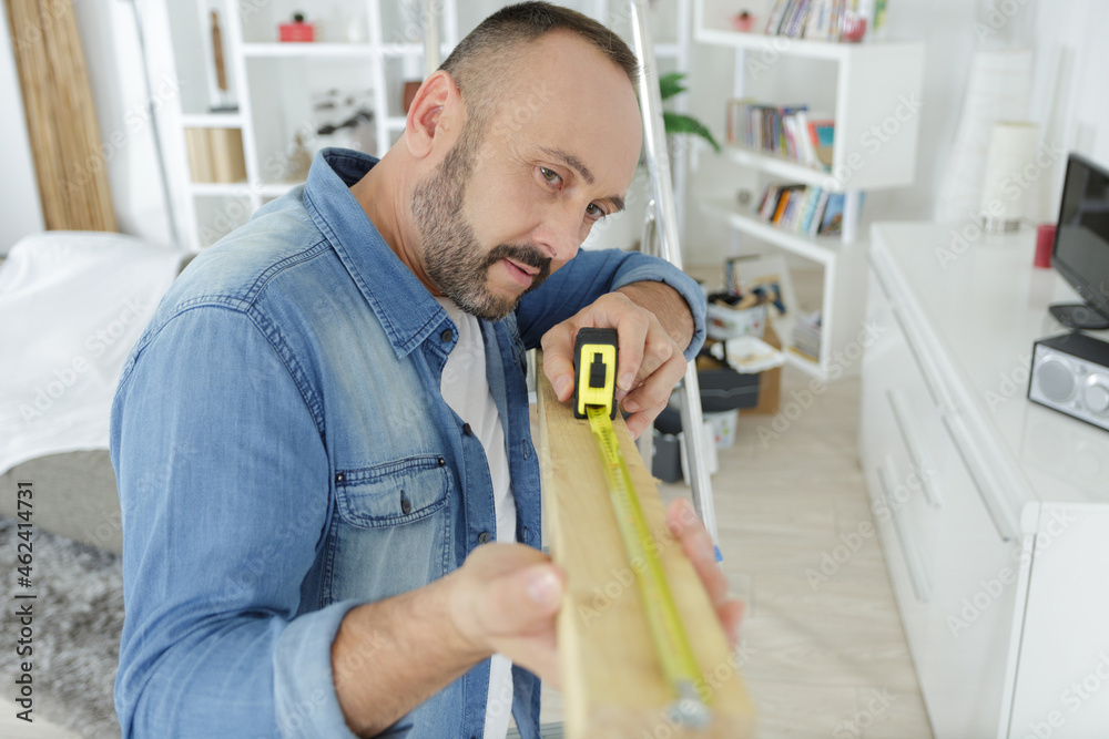 man measuring length of wood in his living room man measuring length of wood in his living room