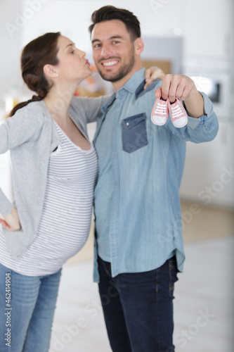 beautiful pregnant woman and her handsome husband holding baby shoes