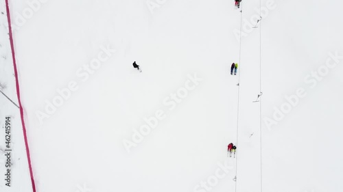 Close up top view from drone on cable way in ski resort. Ski lift elevator transporting skiers and snowboarders on snowy winter slope at mountain resort