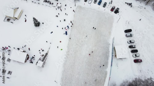 A winter ice rink filmed by a drone on a sunny frosty day. Children and adults, hockey players skate on the ice.