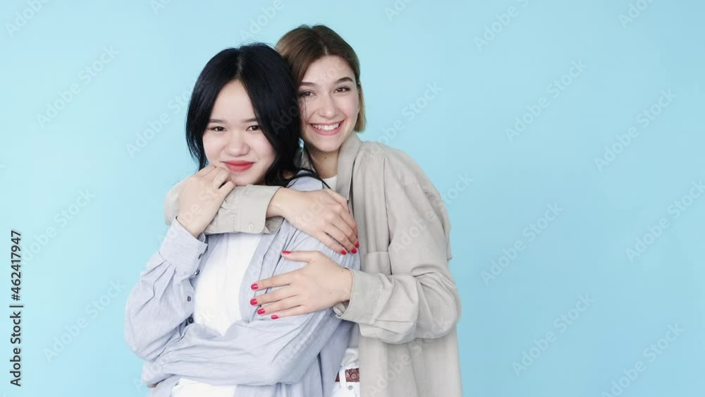 Diversity friendship. Multiethnic friends. Stop Asian hate. People support. Happy mixed race Korean Caucasian girls buddies cuddling smiling isolated on blue free space background. Diversity friendship. Multiethnic friends. Stop Asian hate. People support. Happy mixed race Korean Caucasian girls buddies cuddling smiling isolated on blue free space background.