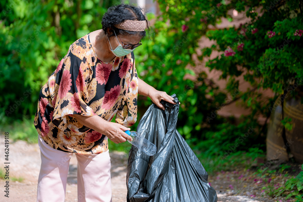 Fototapeta premium Senior woman picking up plastic bottle, garbage collecting in a forest cleaning planet. environment protection pollution problems and global warming, plastic waste caring about nature concept.