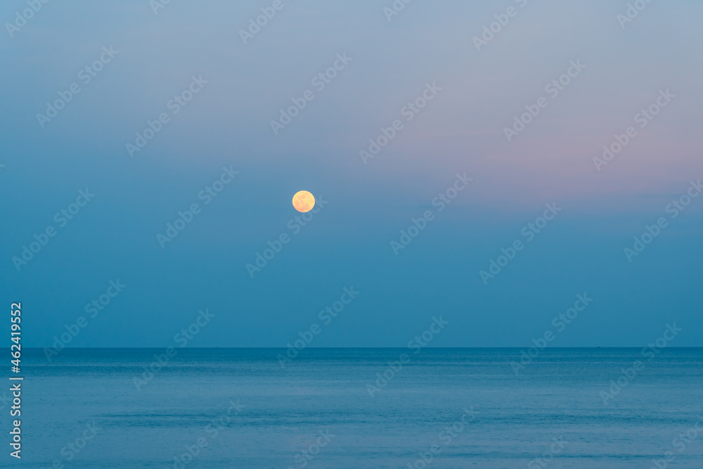 The full moon rises over the sea at a colorful sunset