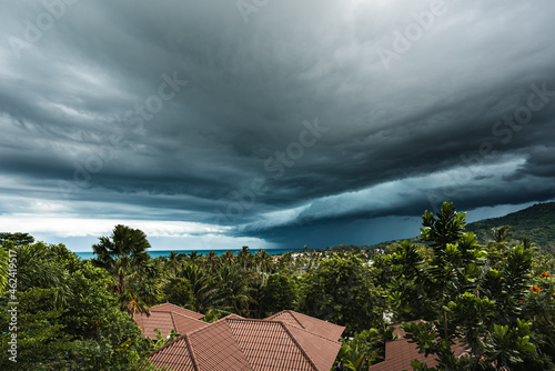Dramatic storm clouds over the sea, forest and rooftops on a summer day