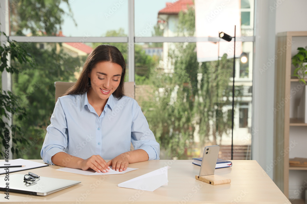 Beautiful young woman making paper plane at desk in office Beautiful young woman making paper plane at desk in office