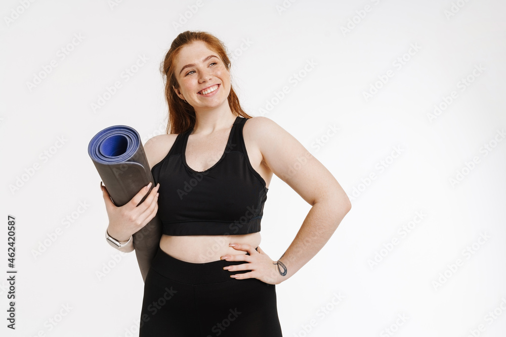 Young ginger woman smiling while posing with fitness mat Young ginger woman smiling while posing with fitness mat