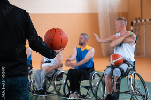 the selector of the basketball team with a disability stands in front of the players and shows them the stretching exercises before the start of training