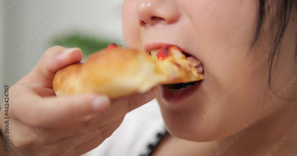 Close up mouth of overweight Asian woman eating junk food slices of pizza at home, addiction to unhealthy fast food, plump female having fun enjoy eating. Close up mouth of overweight Asian woman eating junk food slices of pizza at home, addiction to unhealthy fast food, plump female having fun enjoy eating.