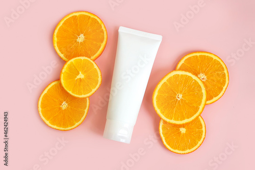 Flacon for cream and orange slices on light pink background. Container for body lotion, toiletry. Tube for professional care products. Skincare and advertising concept. Mockup style, template