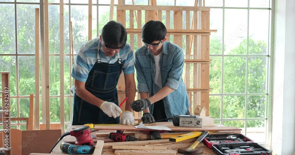 Middle age carpenter man with Asian young man working at workshop room at home to making premium masterpiece carpentry. Middle age carpenter man with Asian young man working at workshop room at home to making premium masterpiece carpentry.