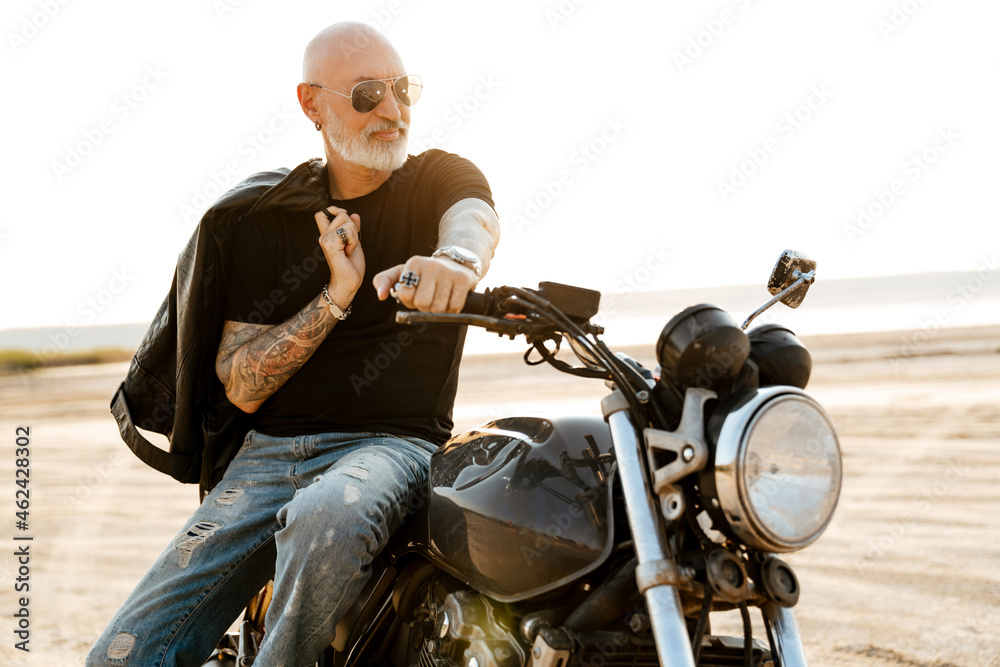Bold senior man with tattoo posing on motorcycle outdoors