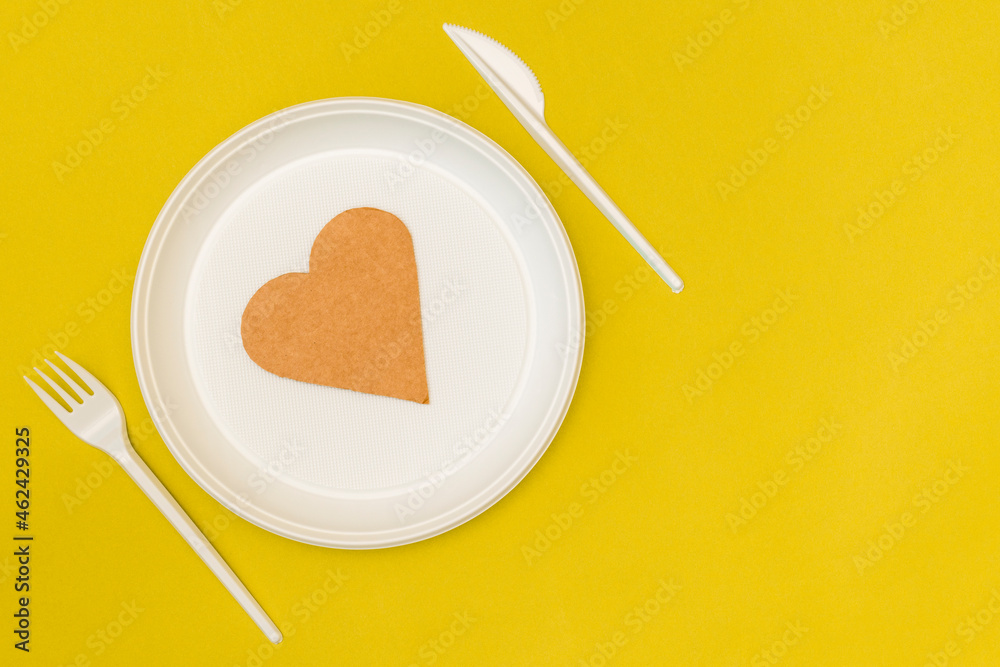 Fork, knife and plate with paper heart on yellow background Fork, knife and plate with paper heart on yellow background