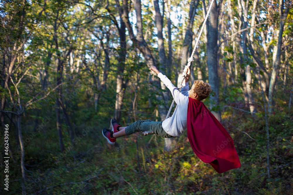 A boy on a rope swing in a red raincoat as Superman