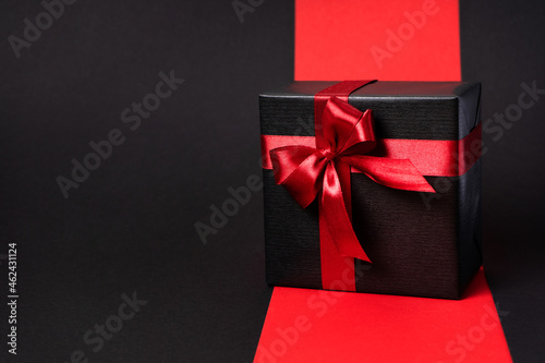 A gift wrapped in dark black paper with a luxurious bow on an even background. With place for text