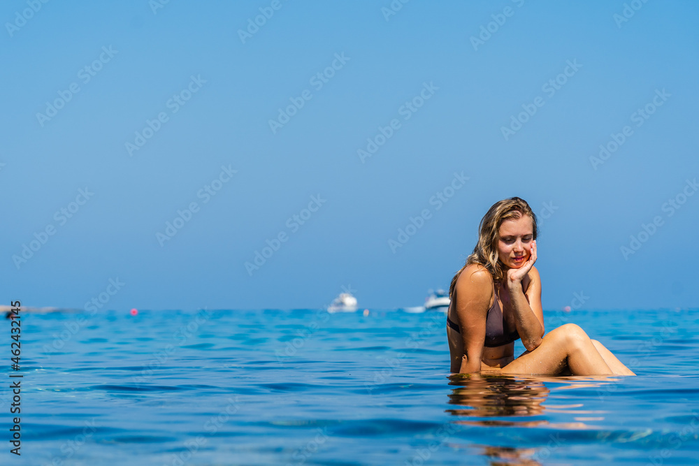 Beautiful woman sits on stone around the clear water of the Sea