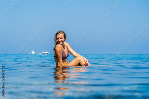 Beautiful woman sits on stone around the clear water of the Sea