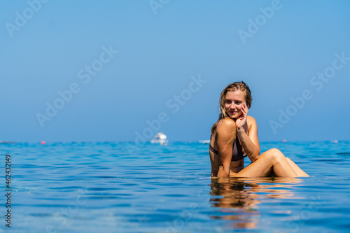 Beautiful woman sits on stone around the clear water of the Sea