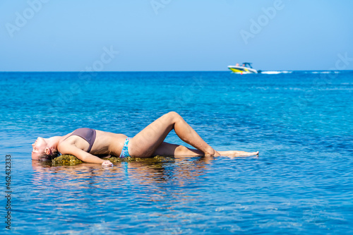 Pretty woman relaxing on stone around the clear azure sea