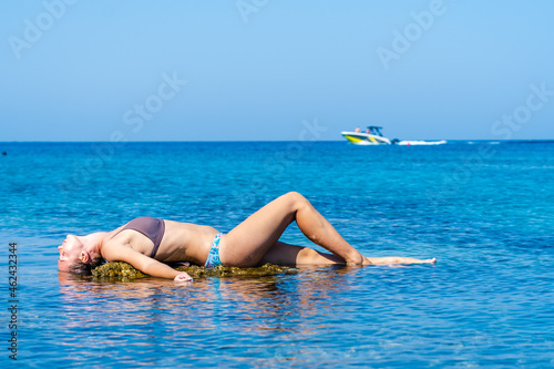 Pretty woman relaxing on rock near the clear blue sea