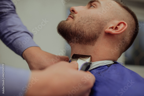 Close up portrait of handsome young man getting beard shaving with straight razor. Focus on the blade. Selective focus