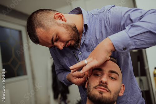 Close up portrait of handsome young man getting beard shaving with straight razor. Focus on the blade. Selective focus