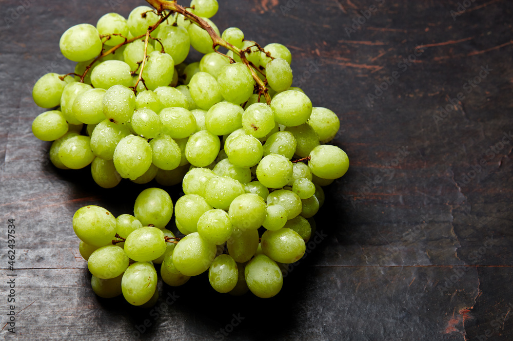 Branch of ripe green grape with water drops. Juicy grapes on wooden background, closeup. Grapes on dark kitchen table with copy space Branch of ripe green grape with water drops. Juicy grapes on wooden background, closeup. Grapes on dark kitchen table with copy space