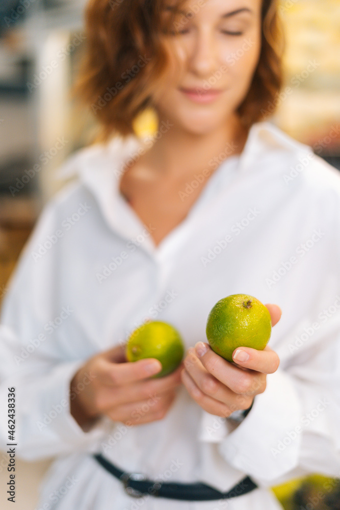 Close-up vertical shot of pretty young adult woman holding in hands lime posing standing at fruit and vegetables section of grocery store, selective focus, blurred background Close-up vertical shot of pretty young adult woman holding in hands lime posing standing at fruit and vegetables section of grocery store, selective focus, blurred background