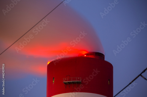 Evening picture of the coal-fired power plant. Blurry view for the smoke coming out of the chimneys. Red light on top of the stack. Photo taken in evening under natural lighting conditions.