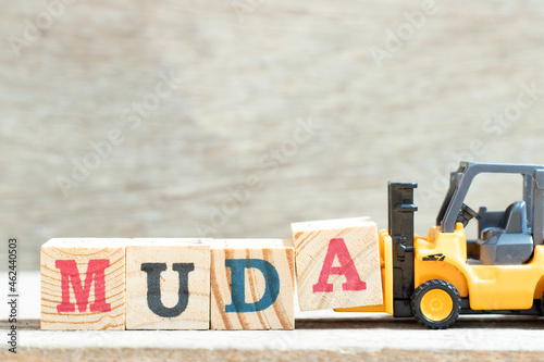 Toy forklift hold letter block A to complete word muda on wood background photo