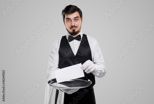 Stylish waiter with empty paper on gray background