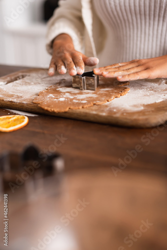 Cropped view of african american woman holding cookie cutter on dough near dry orange slice in kitchen