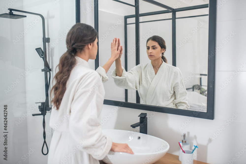 Obraz premium A dark-haired young girl in a white bathrobe in the bathroom