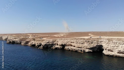 A dusty devil, a tornado on a sandy steep bank rages through a dry bush. Aerial view of steppe dusty terrain coast tourists. Natural phenomena photo