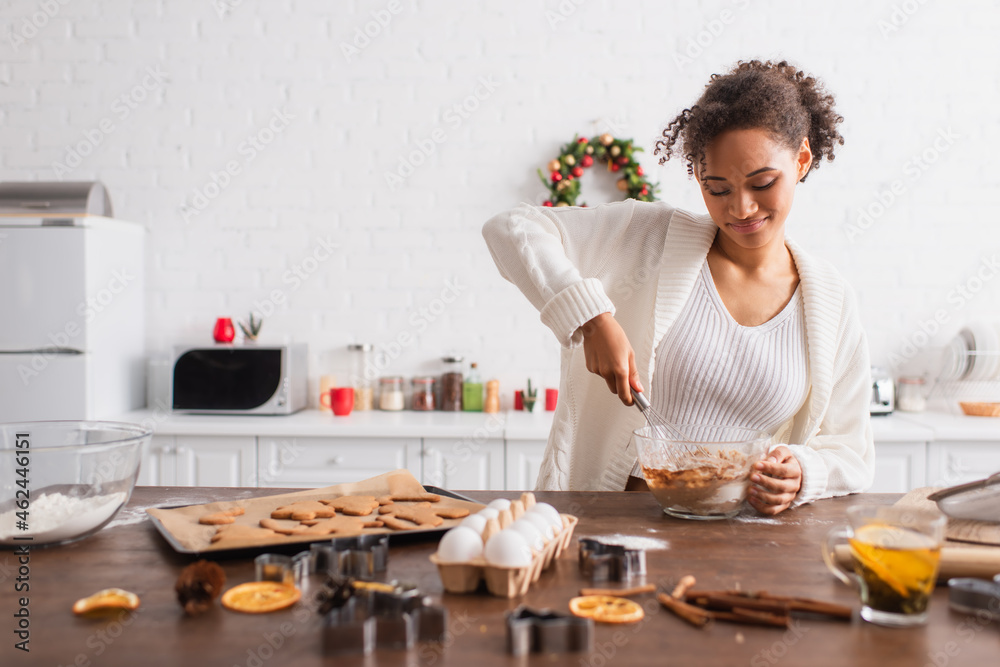 Smiling african american woman cooking near ingredients and christmas cookies in kitchen Smiling african american woman cooking near ingredients and christmas cookies in kitchen