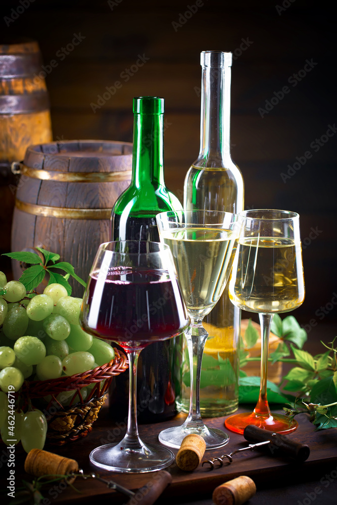 White and red wine, in a bottle and glass on a background of an oak barrel, grapes and kitchen accessories.