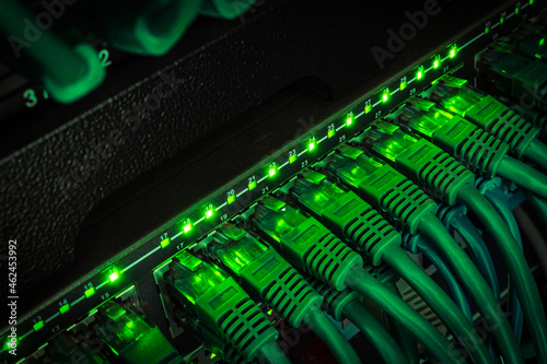 Close up of green network cables from data center connected with patch cord to black switch glowing in the dark