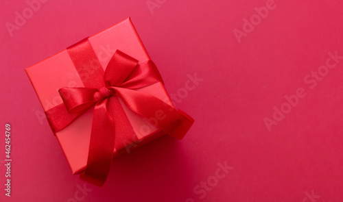 Gift box red ribbon and bow on red background, Christmas present satin curly decoration,
