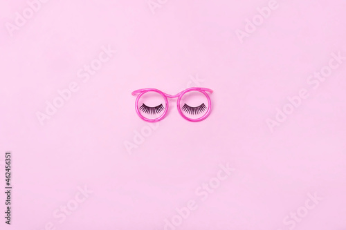 Creative makeup concept with pink glasses, eyelashes and orchid flowers on the pink background. Makeup concept.