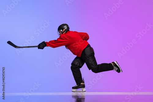 Photography Full-length side view portrait of woman, professional hockey player in motion, training isolated over gradient blue purple background