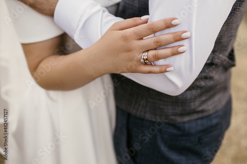 Embrace of the bride and groom at the wedding ceremony on the wedding day. Hands of the bride with a neat beautiful manicure and gold rings with diamonds close-up. Newlyweds in stylish wedding clothes