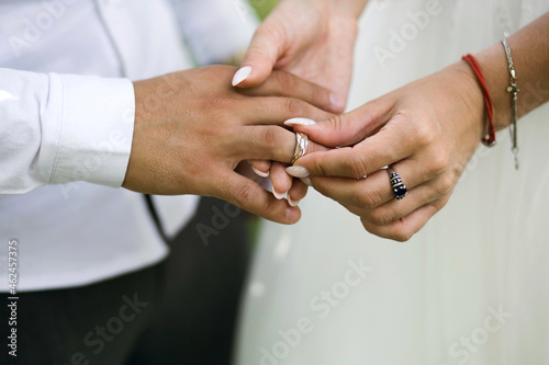 At the wedding ceremony, the bride puts the wedding ring on the groom's finger, side view. Hands of newlyweds with rings close-up. Traditional wedding ceremony with putting on gold rings