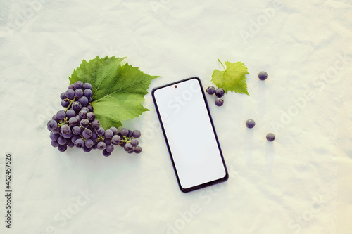 Mockup of an electronic device of a modern smartphone with a bunch of grapes on a beige background. Sunset. Top view