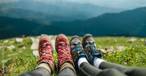 Young couple camping in mountain. Tourists feet in trekking boots relaxing after a long hike on the top of hill on sunny day. Vacation and travel. Carpathians, Ukraine