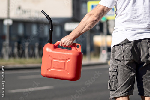 A red canister on the asphalt near the car. The car ran out of gas and stalled. A young man hoping for help on the road from other drivers.