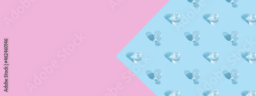 Glasses with water and shadow pattern on blue-pink background banner format with copy space © Alina