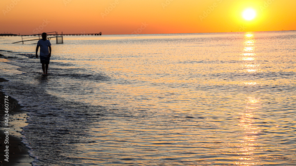 Fototapeta premium Young man walking on the beach at sunset